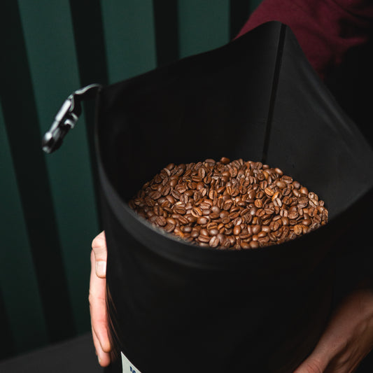 A black reusable food packaging bag for large wholesale B2B deliveries, full of coffee and with a label featuring coffee roastery branding.