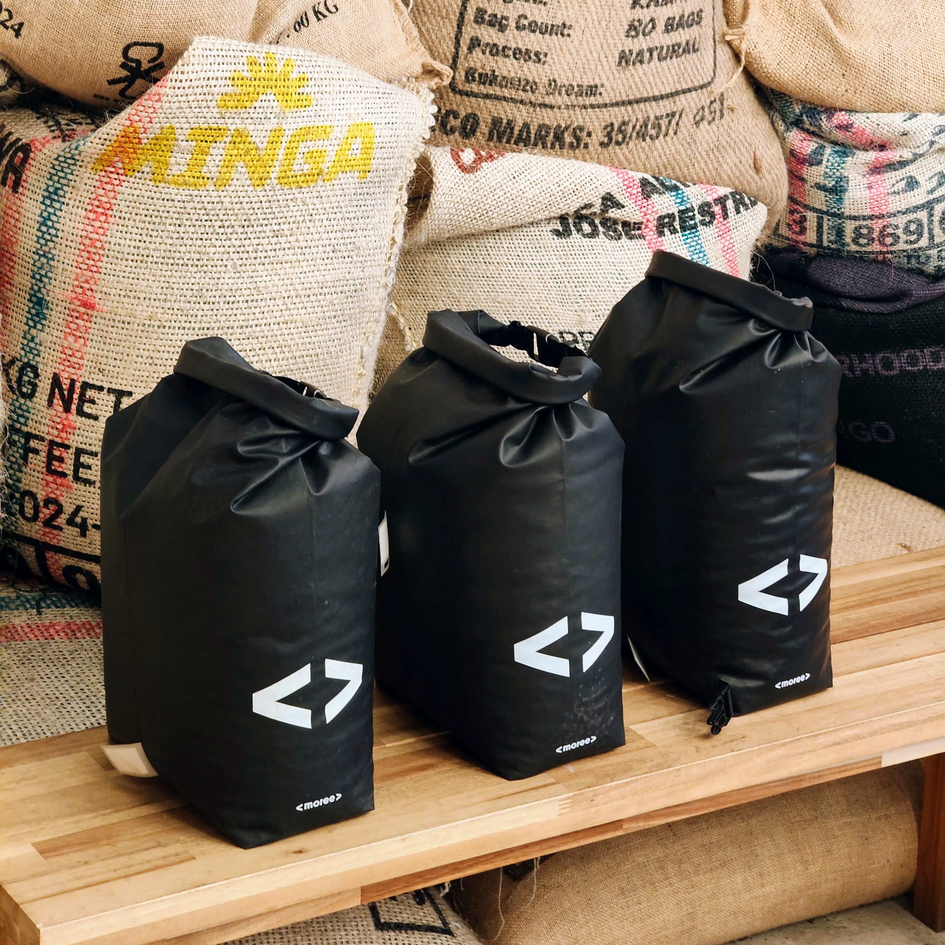 Black reusable bags with a logo on a wooden surface with coffee bags in the background